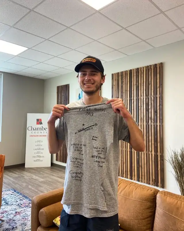 Student pilot holding a signed First Solo 7A3 t-shirt in front of a Chambers County sign