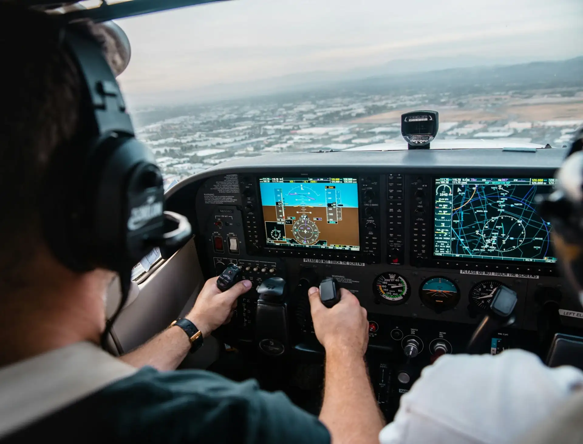 A pilot holding the yoke inside a cockpit equipped with a Garmin G1000 glass panel display during a flight over a residential area at Peachtree City, Georgia